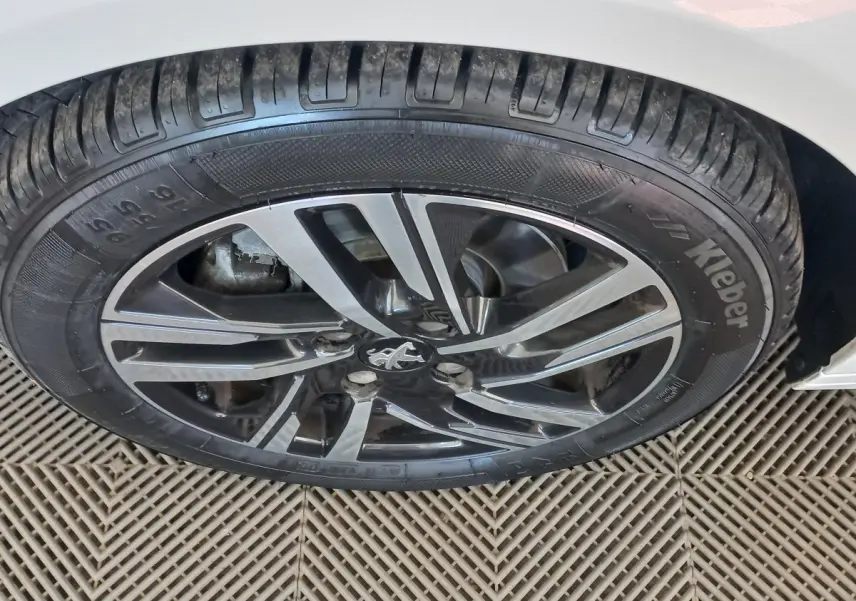 Gros plan sur la roue avant droite d'une Peugeot 208 blanche avec jante alliage au design moderne.