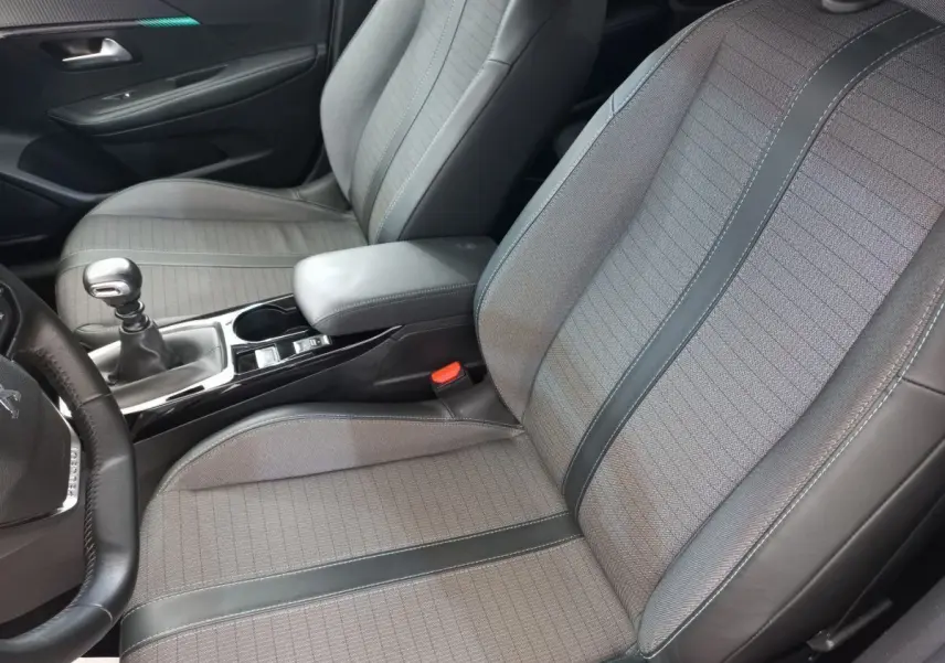 Vue intérieure rapprochée des sièges avant gris et noir d'une Peugeot 208 PureTech 100 S&S Allure 2021 avec levier de vitesse manuel.