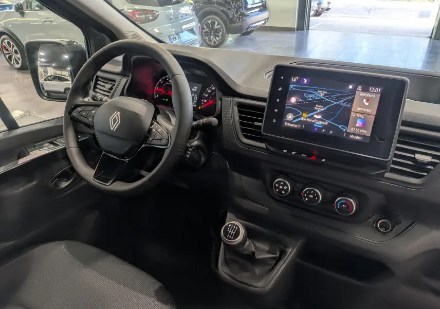 Vue intérieure côté conducteur du Renault Trafic Combi 2025, tableau de bord noir avec écran tactile et levier de vitesses manuel.