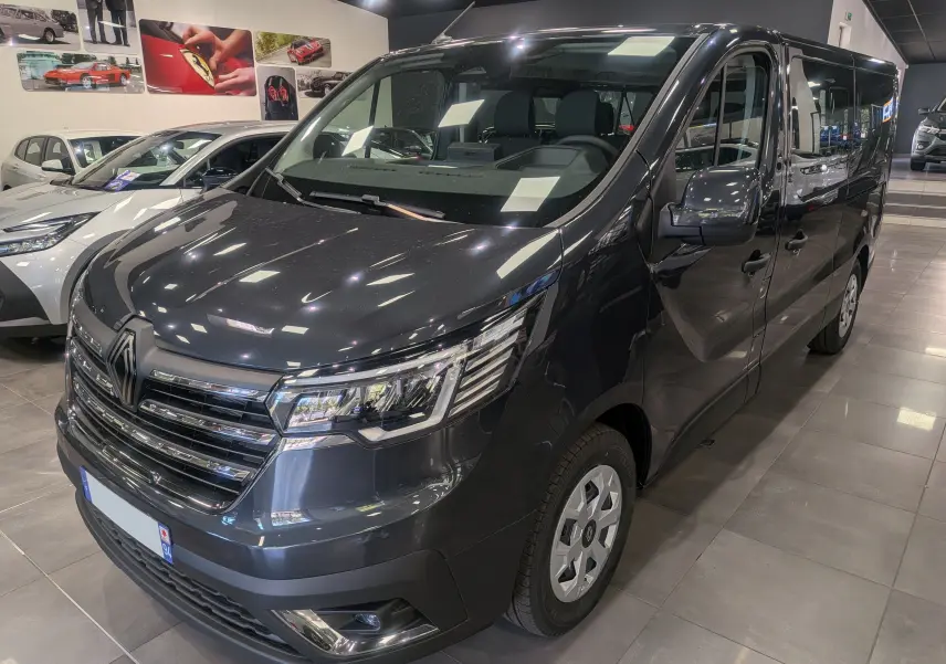 Renault Trafic Combi gris Comète vu en 3/4 avant droit dans un showroom avec reflets sur la carrosserie.