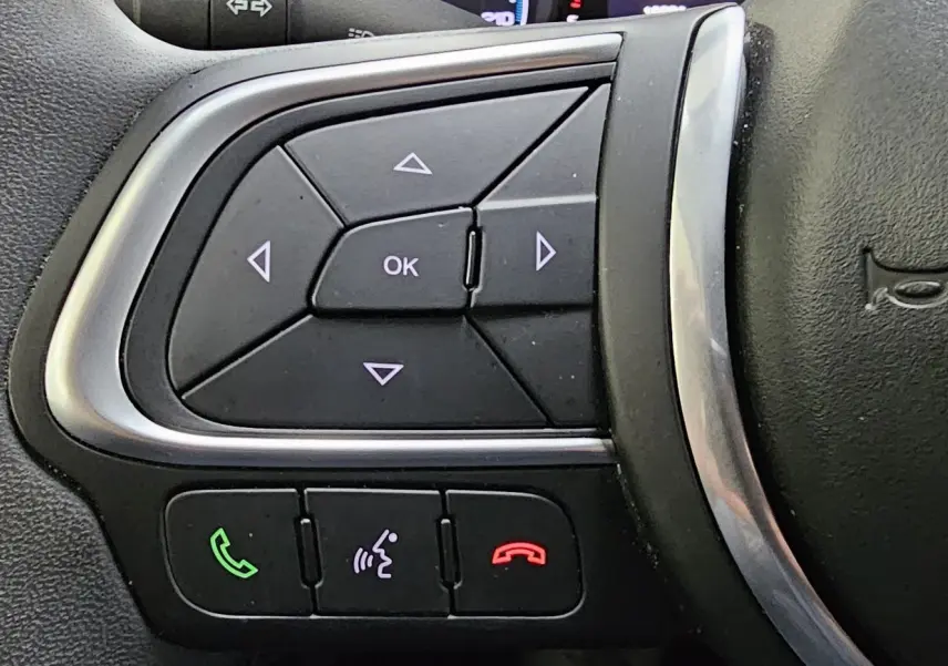Gros plan sur les commandes multifonctions du volant noir du FIAT 500X hybride 2024, avec boutons d'appel et navigation.