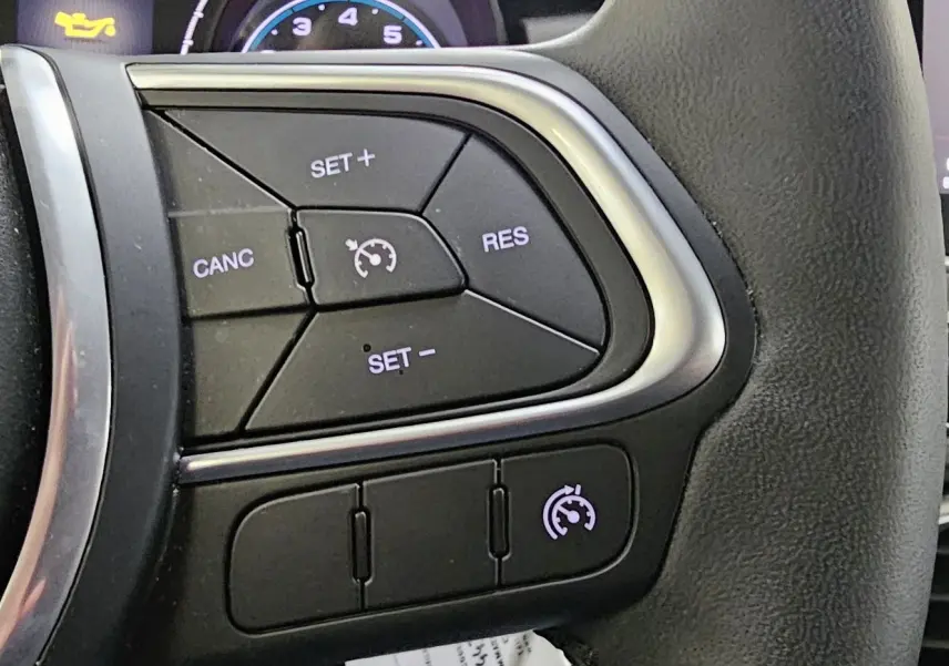 Gros plan sur les commandes de régulateur de vitesse au volant d'une FIAT 500X hybride 2024, intérieur noir.