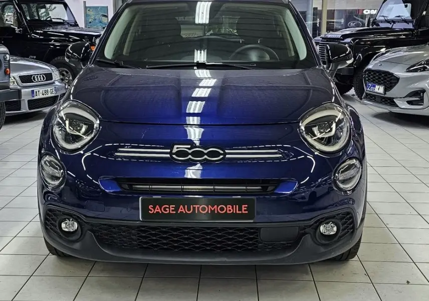 Vue frontale d'une FIAT 500X 2024 bleu profond avec logo 500 centré et phares ronds distinctifs dans un showroom.