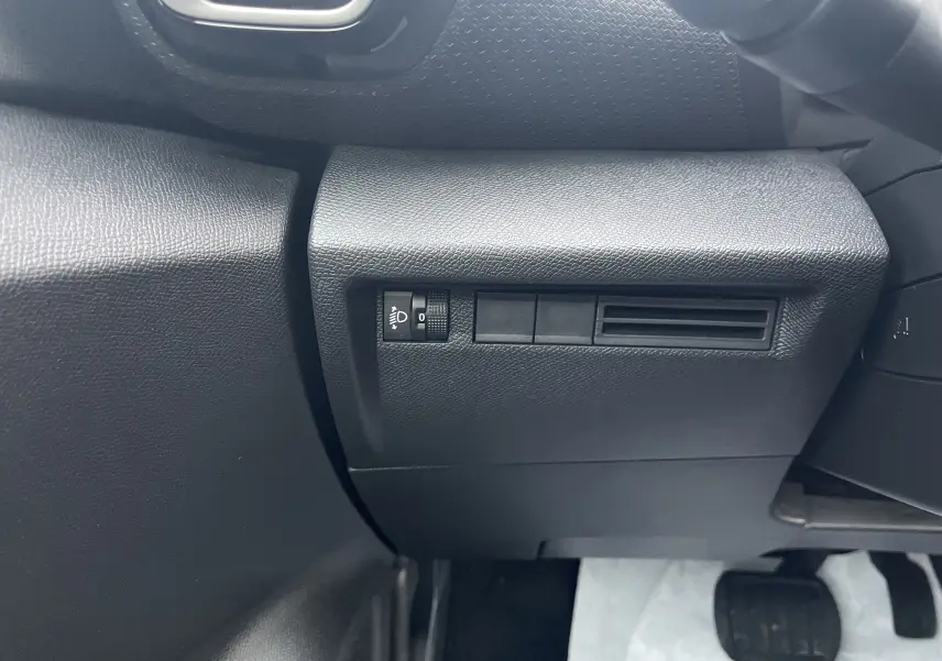 Détail intérieur côté gauche du tableau de bord noir avec commande de réglage des phares sur Citroën C4 hybride 2025.