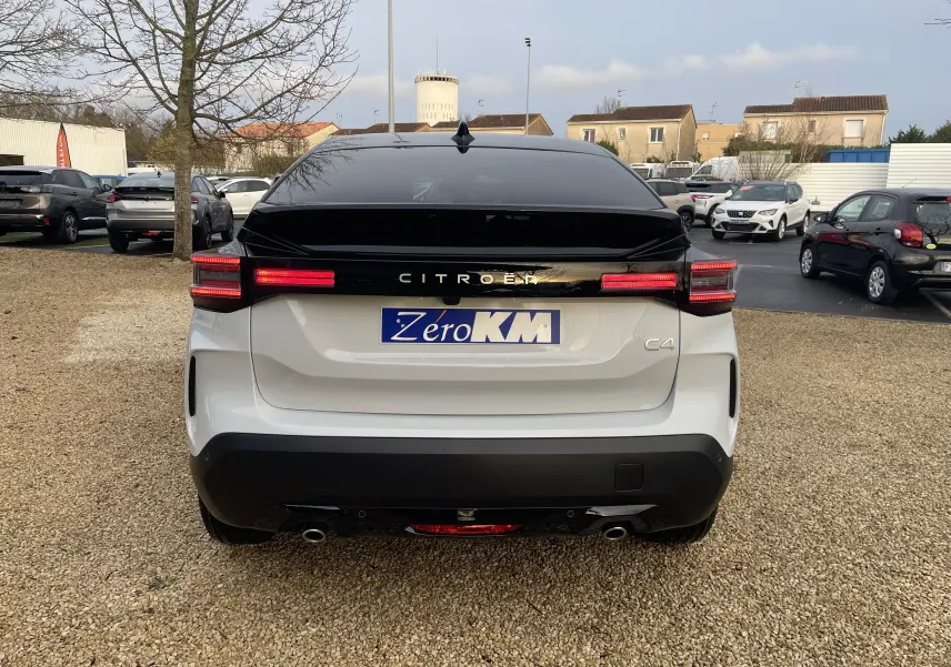 Vue arrière du Citroën C4 2025 blanc Okenite avec toit noir Perla, feux LED allumés et double sortie d’échappement.