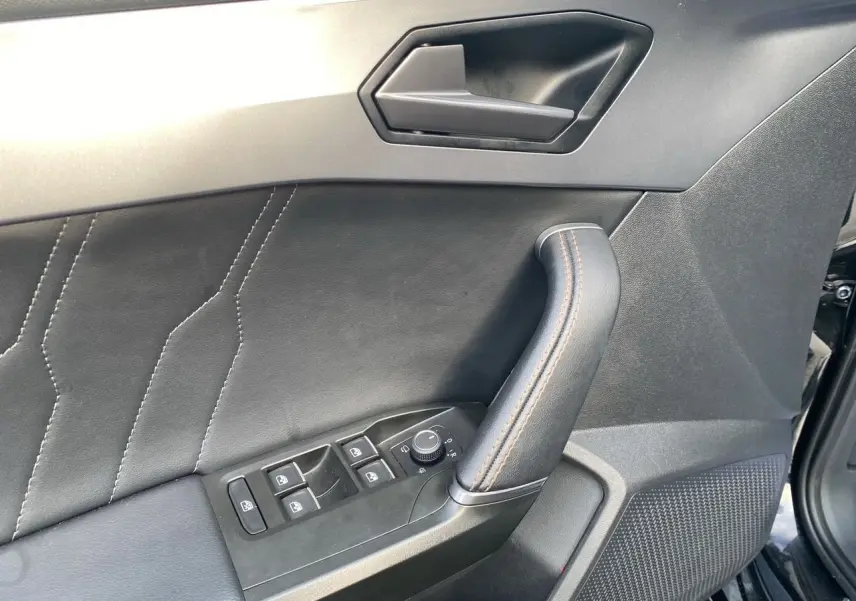 Détail de la porte avant gauche noire de la CUPRA Leon 2023 avec commandes des vitres et poignée en cuir.