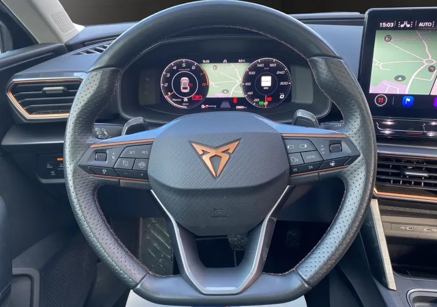 Vue rapprochée du volant noir perforé de la CUPRA Leon 2023 avec tableau de bord numérique et écran tactile de navigation.