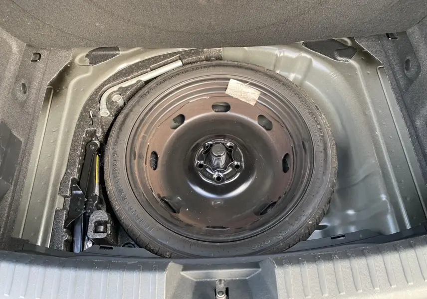 Vue plongeante sur la roue de secours noire et le cric dans le coffre d'une CUPRA Leon 2023.