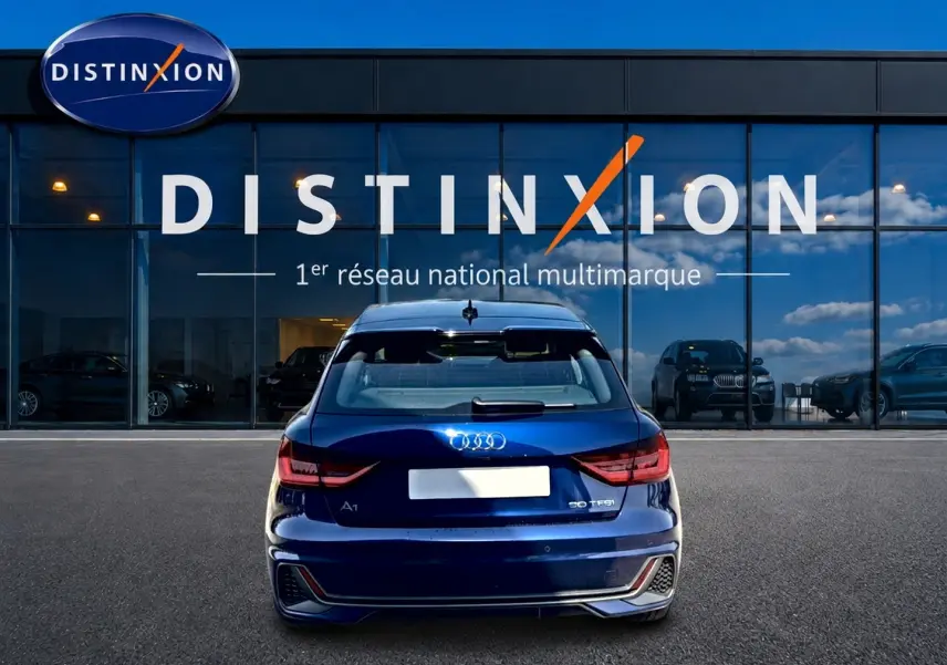 Vue arrière d'une Audi A1 Sportback 30 TFSI bleu foncé avec feux LED, garée devant une vitrine Distinxion.