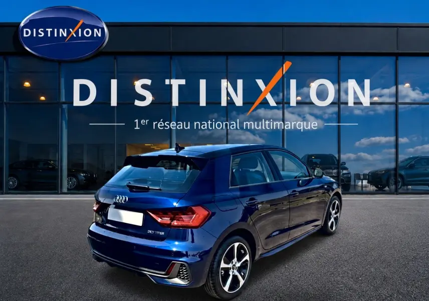 Audi A1 Sportback bleu 3/4 arrière droit, avec jantes alu et becquet arrière visible devant showroom Distinxion.