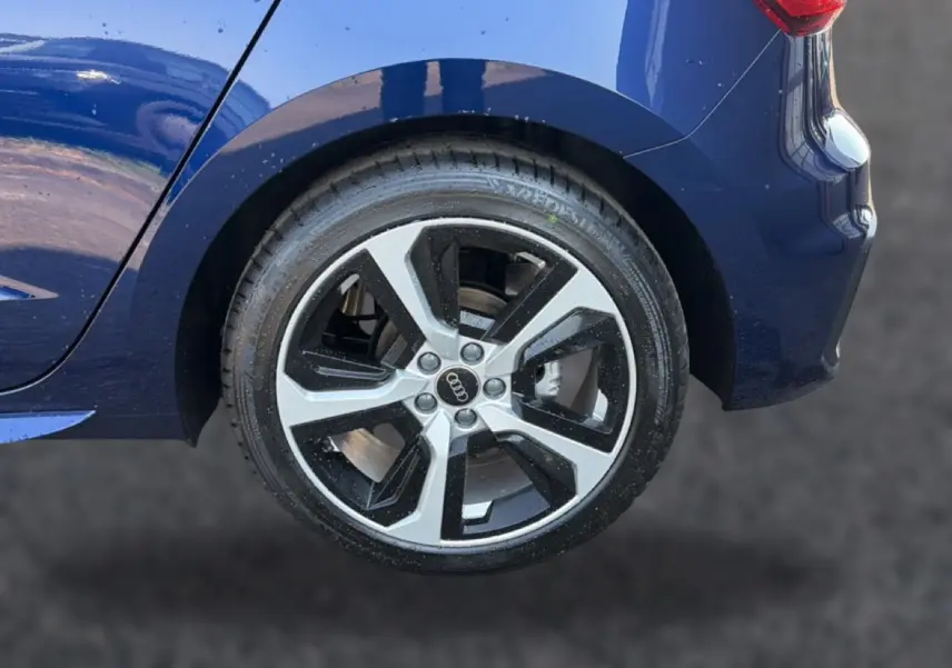 Gros plan sur la roue arrière droite d’une Audi A1 Sportback bleu foncé avec jante alu bicolore et partie arrière du véhicule visible.