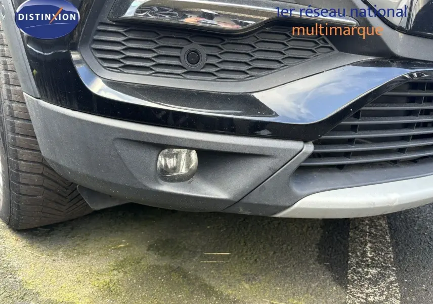 Gros plan sur le pare-chocs avant noir d'un Opel Grandland X 2019, mettant en valeur la calandre et le feu antibrouillard.