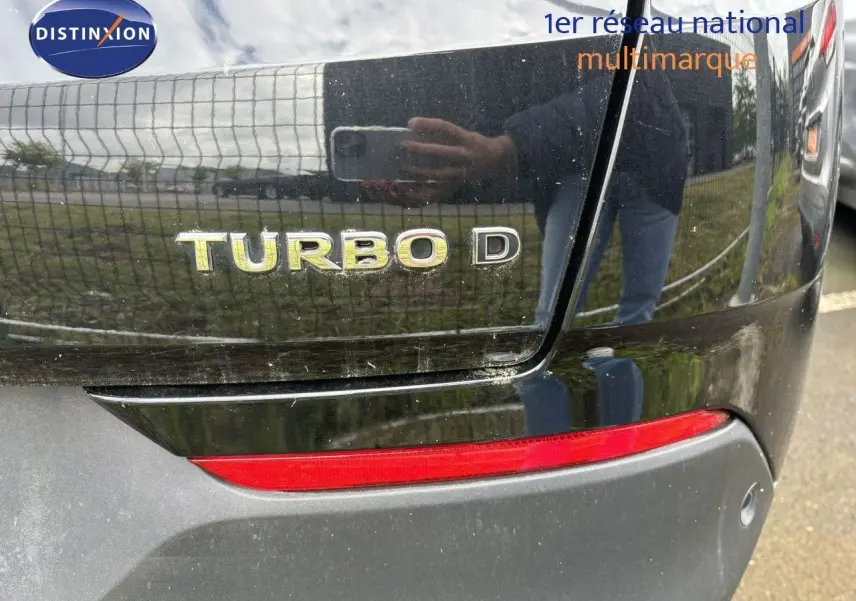 Gros plan sur le logo Turbo D à l'arrière d'un Opel Grandland X noir, avec feu arrière rouge visible.