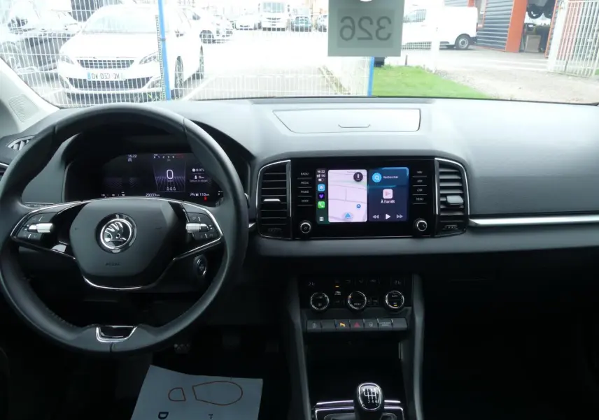 Vue intérieure frontale du tableau de bord du Skoda Karoq blanc 2024 avec écran tactile et volant multifonctions noir.