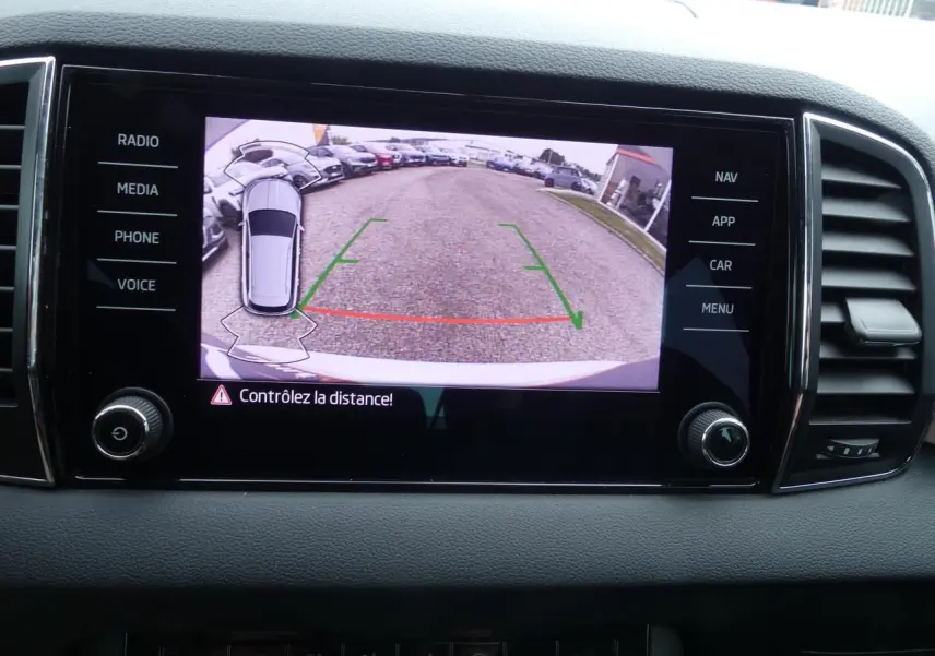 Écran tactile du tableau de bord montrant la caméra de recul avec vue arrière et alertes de distance du Skoda Karoq blanc.