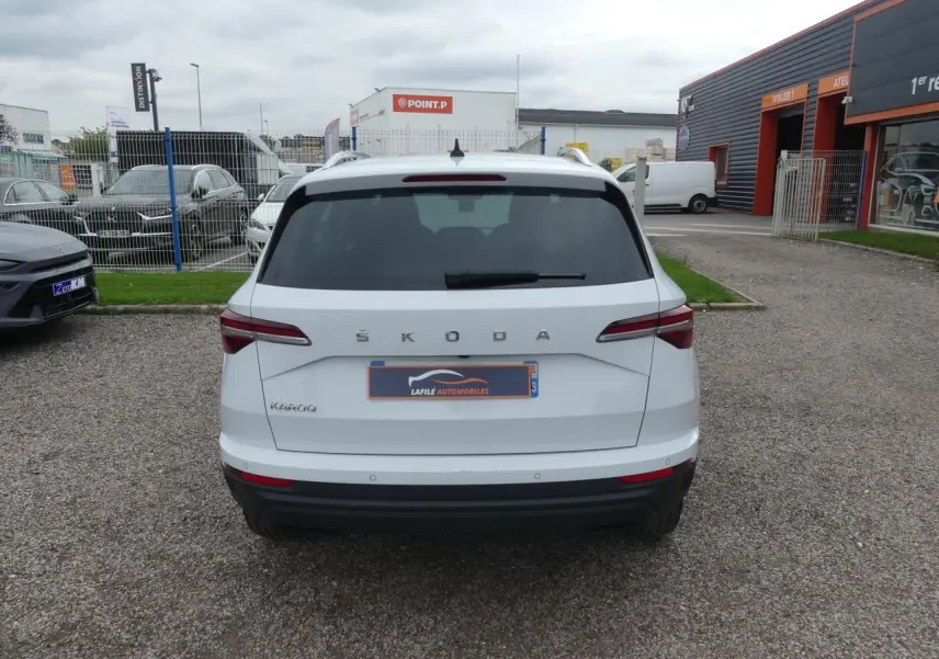 Vue arrière d'un SUV SKODA KAROQ blanc avec feux arrière LED et logo ŠKODA visible sur un parking.