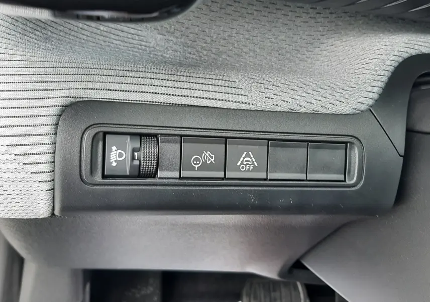 Gros plan sur les commandes de réglage des phares et d’aide à la conduite sur la planche de bord grise du Citroën C3 Aircross hybride 2025.