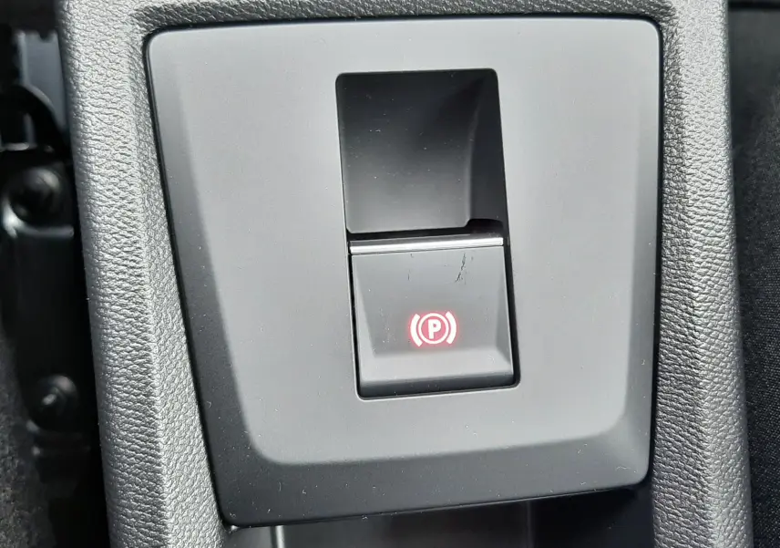 Gros plan sur le bouton de frein à main électronique rouge dans la console centrale d'une Citroën C3 Aircross hybride gris toit noir.
