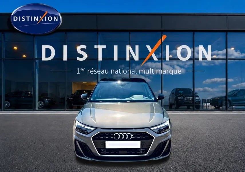 Vue avant d'une Audi A1 Sportback gris chronos avec calandre noire et logo Audi, devant une vitrine Distinxion.