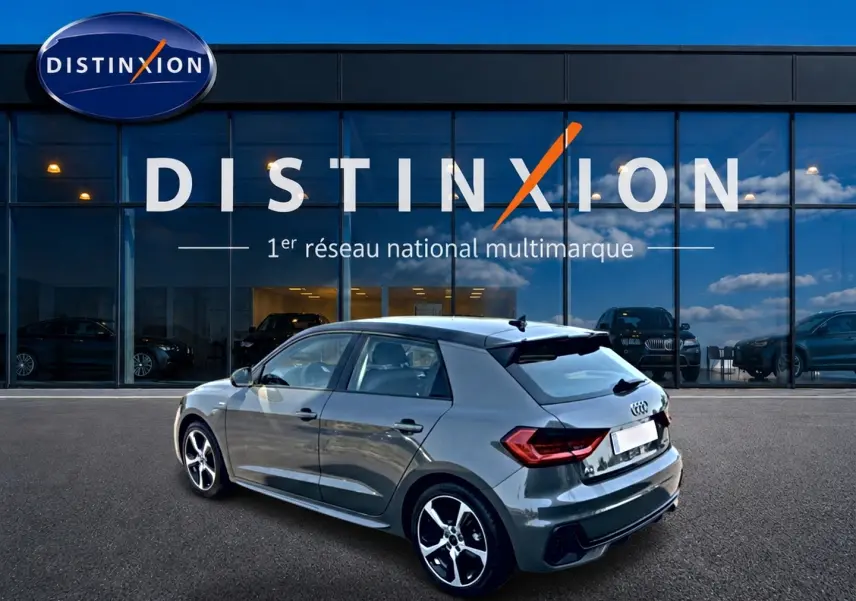 Audi A1 Sportback gris chronos vue 3/4 arrière droit avec jantes alu et becquet noir devant une vitrine Distinxion.