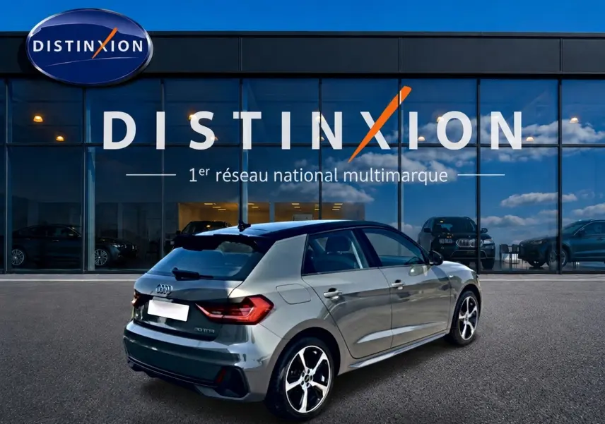 Audi A1 Sportback gris chronos avec toit noir, vue 3/4 arrière droit, stationnée devant une vitrine Distinxion.