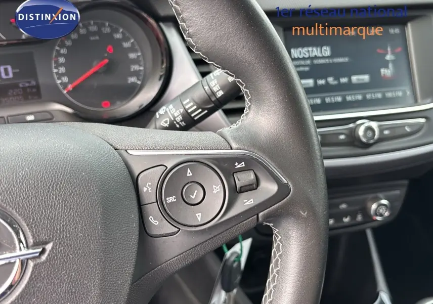 Gros plan sur le volant et la console centrale d'un Opel Crossland X gris Pierre de Lune, mettant en valeur les commandes au volant et l'écran multimédia.