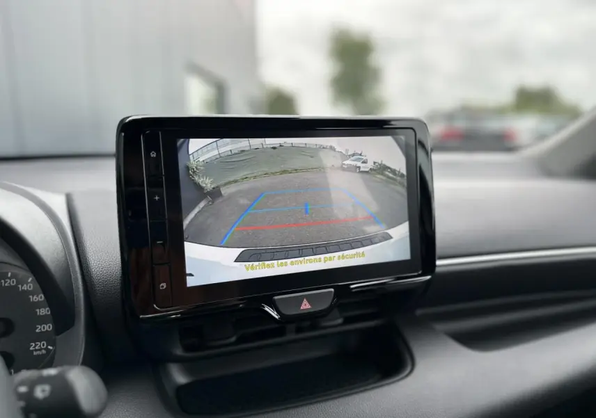 Écran tactile central affichant la caméra de recul d'une Toyota Yaris Hybride blanche, tableau de bord en arrière-plan.