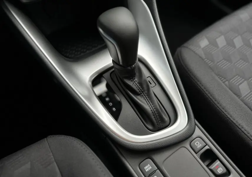 Gros plan sur la console centrale de la Toyota Yaris hybride 2025, avec levier de boîte auto et sellerie tissu noir.