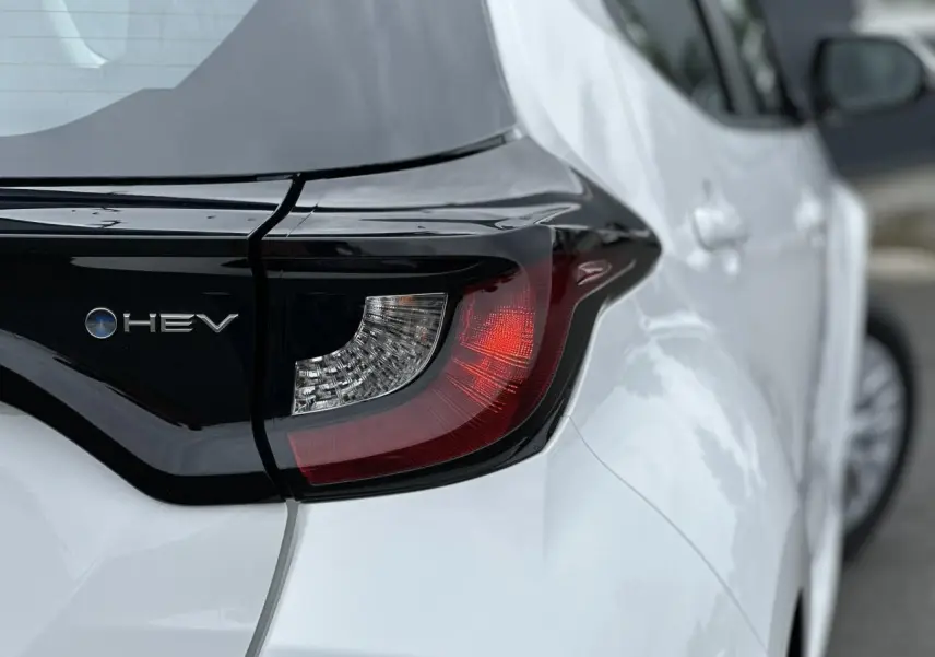 Gros plan sur le feu arrière gauche noir et blanc pur de la Toyota Yaris Hybride 2025 avec logo HEV visible.