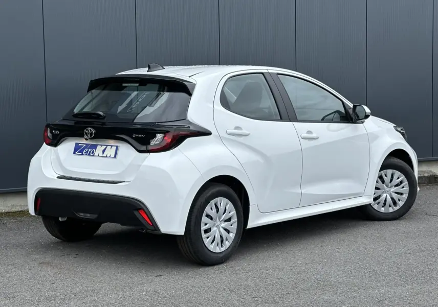 Toyota Yaris hybride blanc pur vue 3/4 arrière droit, avec toit noir et jantes acier à enjoliveurs.