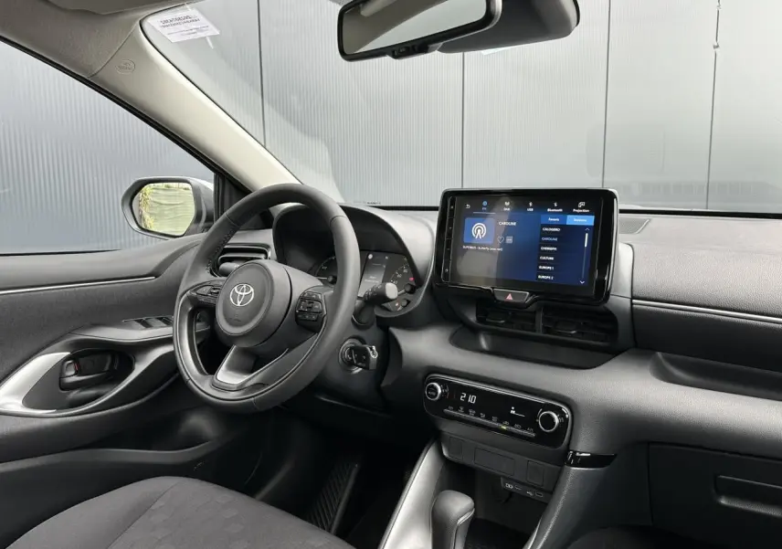Intérieur avant gauche de la Toyota Yaris hybride 2025 avec volant multifonction cuir et écran tactile 9 pouces allumé.