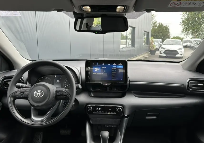 Vue intérieure avant de la Toyota Yaris hybride 2025, tableau de bord noir avec écran tactile central et volant multifonction cuir.