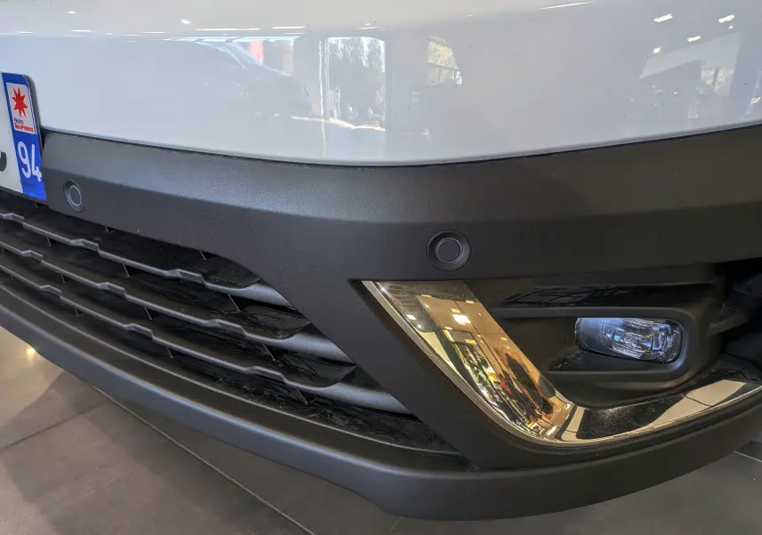 Gros plan sur le pare-chocs avant droit blanc glacier du Renault Trafic Combi avec antibrouillard et capteur de stationnement.