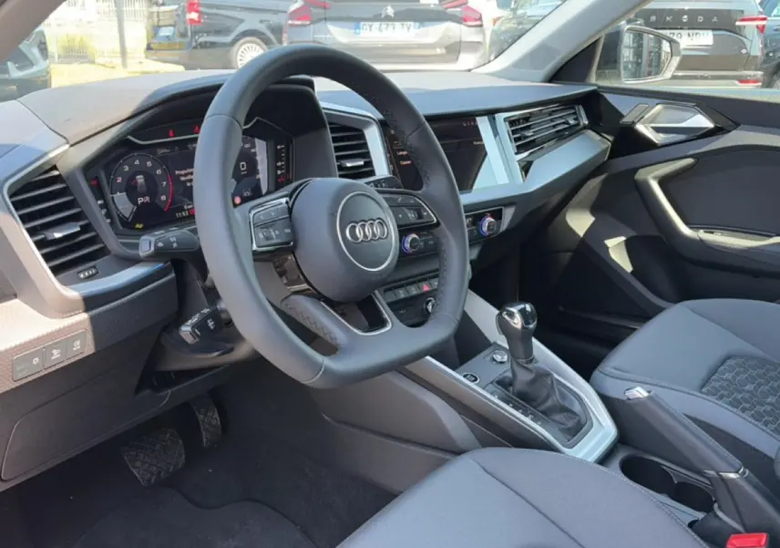 Vue intérieure côté conducteur de l'Audi A1 Sportback 2026, tableau de bord et volant multifonction noirs.