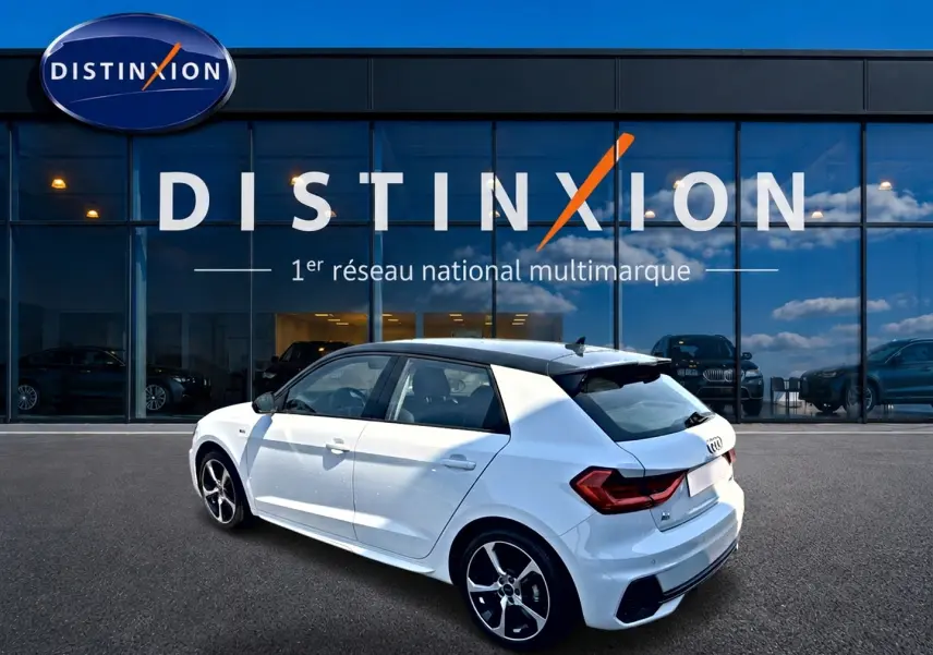 Audi A1 Sportback blanc et noir en 3/4 arrière droit, avec jantes alu et becquet arrière, devant une vitrine Distinxion.