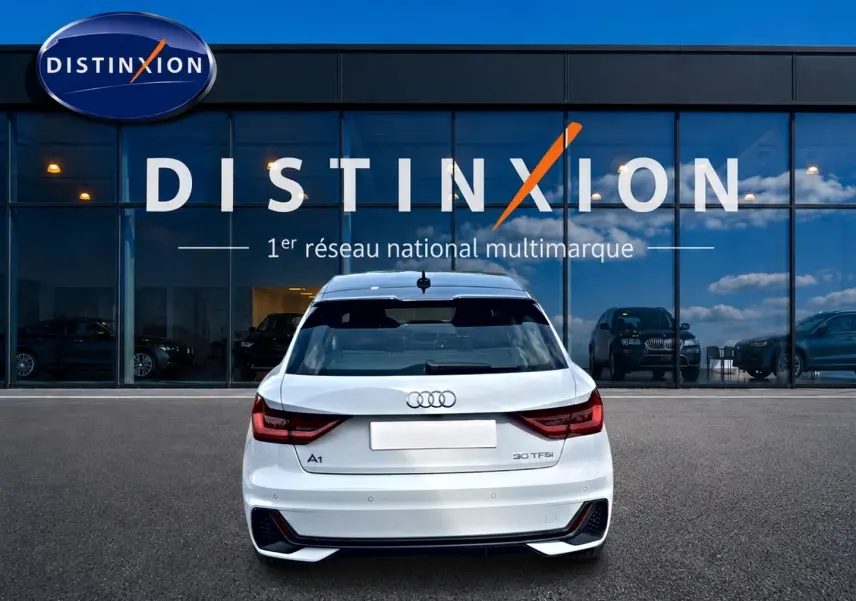 Vue arrière d'une Audi A1 Sportback 30 TFSI blanche avec détails noirs, stationnée devant une vitrine Distinxion.