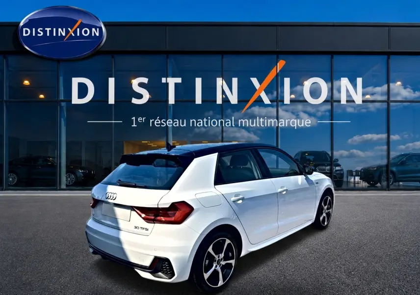 Audi A1 Sportback blanc et noir vue 3/4 arrière droit avec jantes alu et becquet arrière, devant vitrine Distinxion.