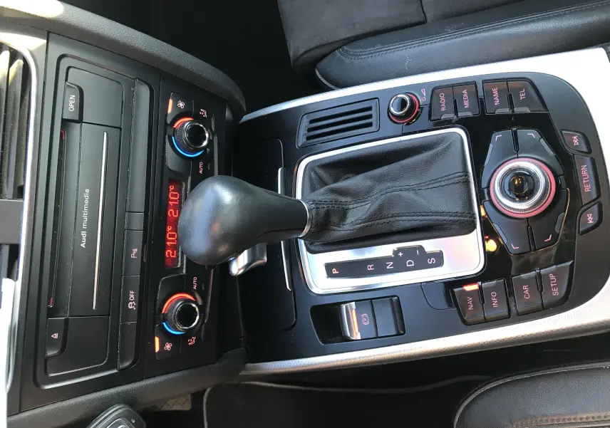 Vue rapprochée de la console centrale noire et argentée avec levier de vitesse automatique et commandes multimédia d'une Audi A5 gris dauphin.