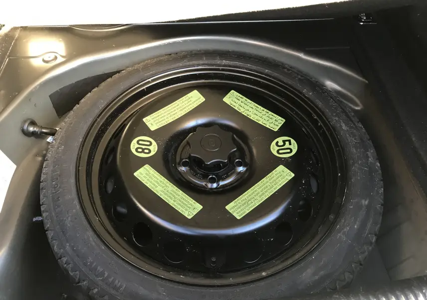 Gros plan sur la roue de secours noire avec étiquettes jaunes dans le coffre d'une Audi A5 gris dauphin de 2012.