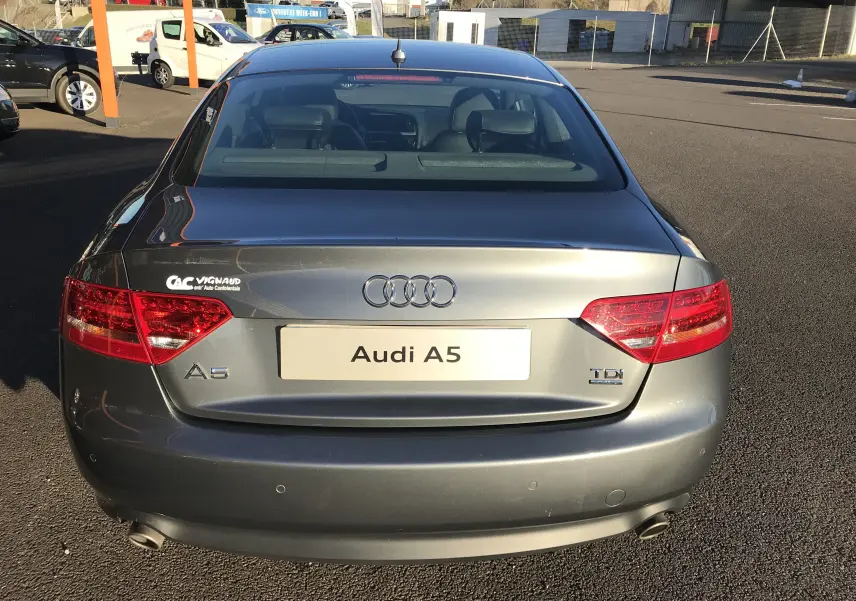 Vue arrière d'une Audi A5 Coupé gris dauphin de 2012 avec feux rouges et double sortie d'échappement visible.
