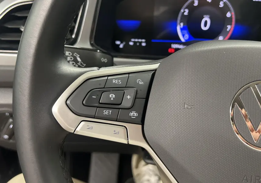 Gros plan sur le volant du Volkswagen T-Roc 2024, boutons de régulateur de vitesse à gauche et logo VW au centre.