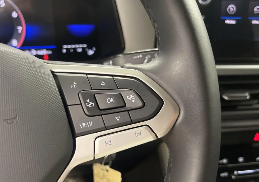 Gros plan sur le volant noir du Volkswagen T-Roc 2024 avec commandes multifonctions et tableau de bord numérique.