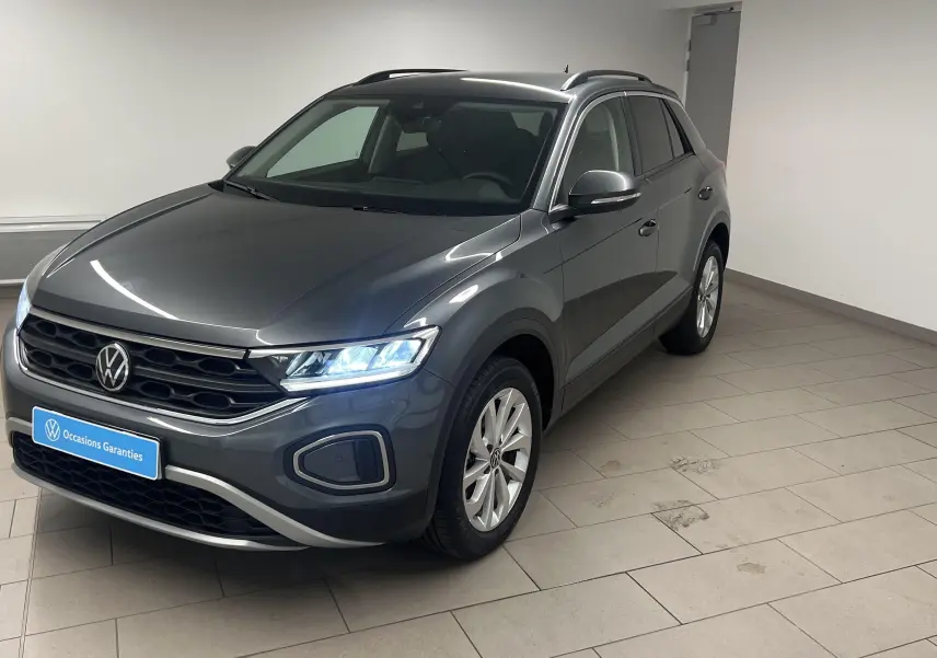 Volkswagen T-Roc gris Indium en 3/4 avant droit, avec jantes alliage 17'' Johannesburg et feux allumés.