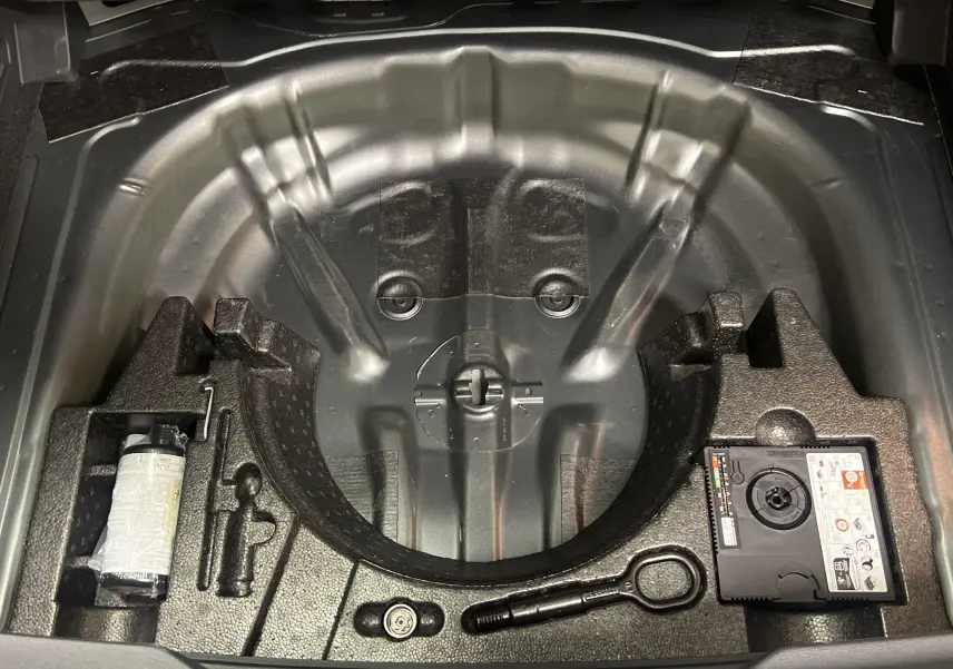 Coffre ouvert montrant le rangement sous plancher du Volkswagen T-Roc gris Indium avec kit de réparation pneus intégré.