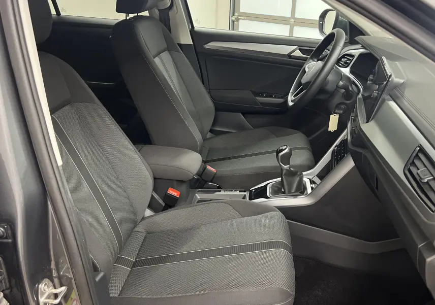 Intérieur avant du Volkswagen T-Roc 2024, sièges tissu gris et console centrale avec levier de vitesses manuel.