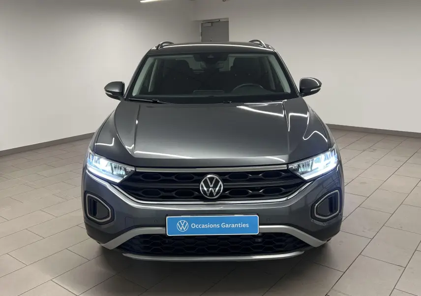 Volkswagen T-Roc gris Indium vu de face avec phares allumés et calandre noire distinctive.