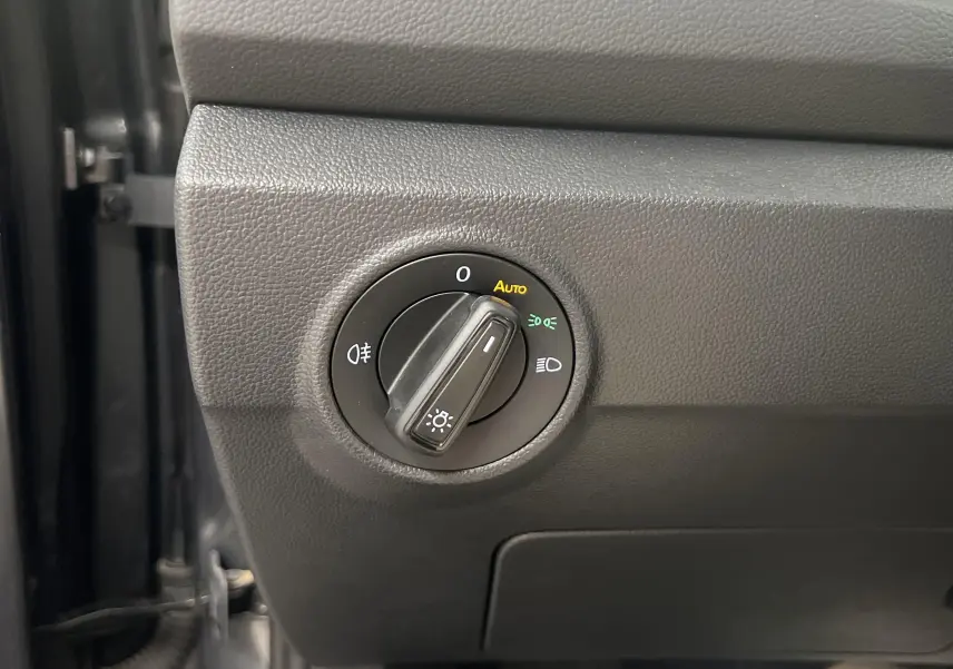 Gros plan sur le bouton de commande des phares du Volkswagen T-Roc 2024, finition gris indium, intérieur côté conducteur.