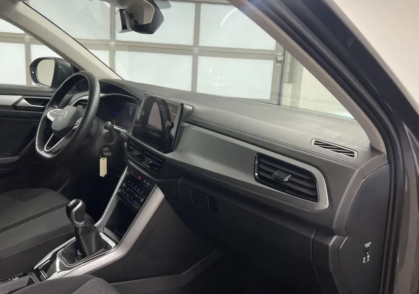 Intérieur du Volkswagen T-Roc 2024 côté conducteur, tableau de bord moderne avec écran tactile et levier de vitesses manuel.