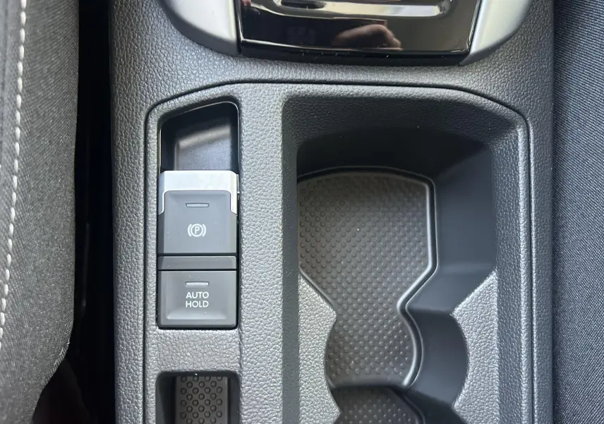 Gros plan sur la console centrale du Volkswagen T-Roc 2024, montrant le frein à main électrique et le porte-gobelets.