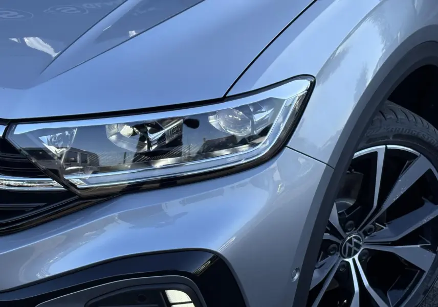 Gros plan sur l'avant droit du Volkswagen T-Roc gris pyrite, mettant en valeur le phare LED et la jante alliage 19 pouces R-Line.